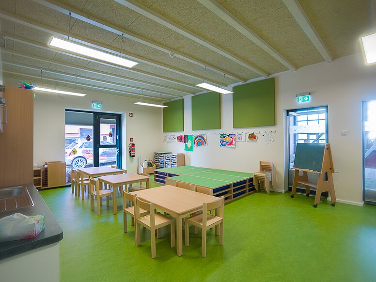 Groepsruimte van het kinderdagverblijf "In der Kammgarnspinnerei". Groepsruimte van een kinderdagverblijf met groene vloer en houten tafels en stoelen